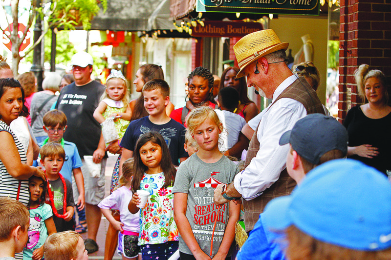 A crowd surrounds magician, comedian and mind reader Derrick Rose composes balloon animals during the First Thursday event in downtown El Dorado. The summer carnival themed festivity included more than a dozen downtown businesses that offered a variety of free games, prizes, giveaways and food, mostly aimed at children. 