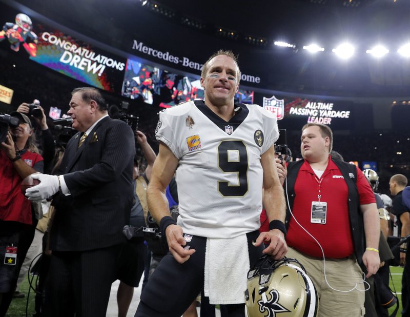 In This Oct. 8, 2018, file photo, New Orleans Saints quarterback Drew Brees (9) reacts after breaking the NFL record for all-time passing yards during, the first half of an NFL football game against the Washington Redskins in New Orleans. Visitors to the Pro Football Hall of Fame can see both the football Drew Brees threw in becoming the NFL's all-time passing yards leader and the uniform the Saints quarterback wore while making history. Mark Baker, the hall's president and chief executive officer, holds the ball at left. (AP Photo/Gerald Herbert, File)