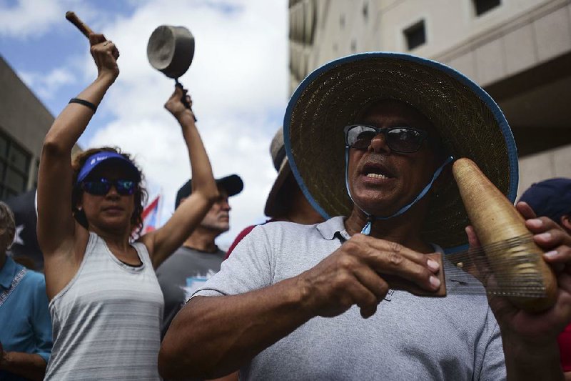 A woman bangs on a pot and a man plays a guiro during a march  Thursday in San Juan to celebrate the resignation of Puerto Rico’s Gov. Ricardo Rossello. 