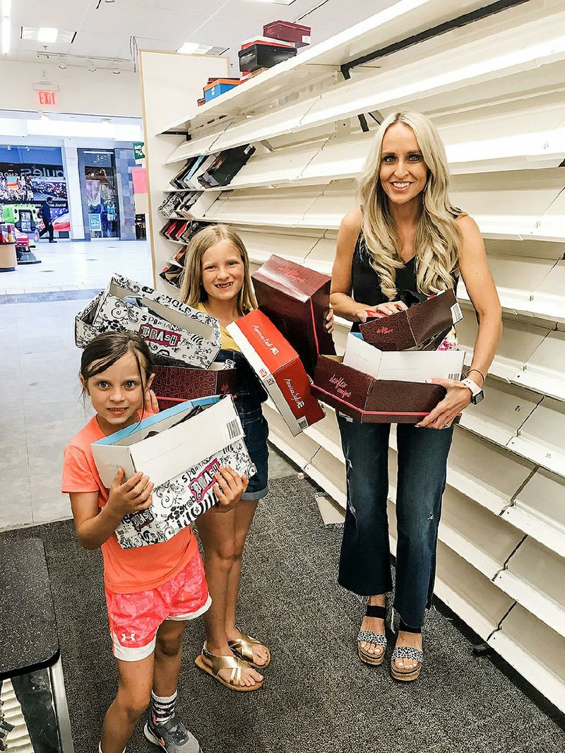 Carrie Jernigan and her daughters — Harper (center), 9, and Campbell, 6 — load shoes from the Payless ShoeSource in Fort Smith’s Central Mall in May after Jernigan bought the entire stock of about 1,500 pairs. Jernigan has been giving the shoes to the needy in the Arkansas River Valley.