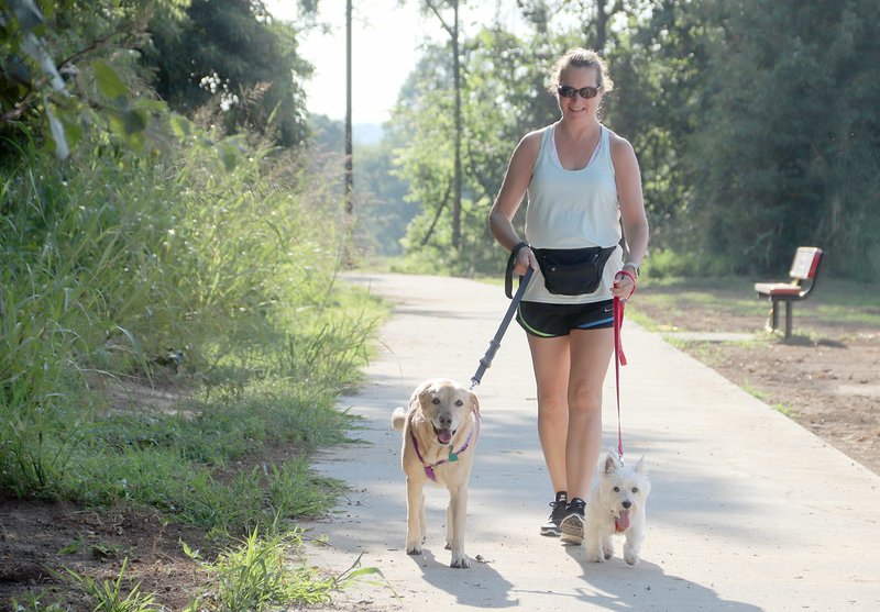 Melodie Hurley, who lives in Fayetteville off Wedington Drive, walks her dogs on the new walking trail at Creekside Park in Farmington. She said she uses the park frequently for exercise. Her dogs are Lily the yellow lab and Ivy the Westie. With the new trail addition, the park now has a combined 1.25-mile public walking trail.
