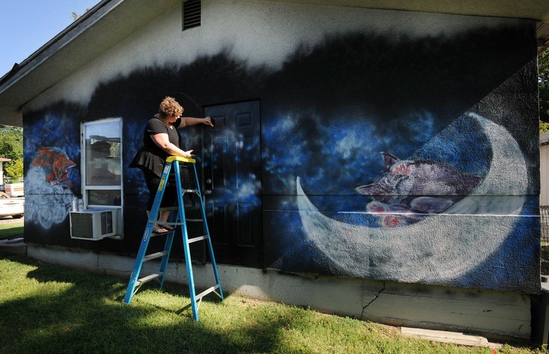 NWA Democrat-Gazette/ANDY SHUPE Shelby Nichols of Rogers paints a fish July 26 on the south wall of the Outback Cat House Rescue in Rogers. Rogers Experimental House donated the paint for the project, and Nichols donated her time. A fundraiser is set up on Facebook to raise money for Nichols and the cat house.