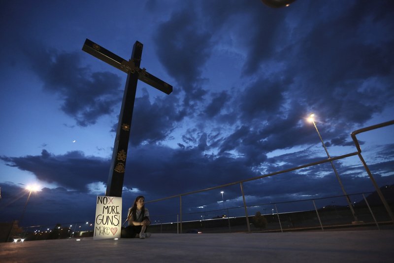 A woman sits next to a sign with a message that reads: &#xa8;No More Guns! Make Love&#xa8;, in Juarez, Mexico, Saturday, Aug. 3, 2019, where people are gathering for a vigil for the 3 Mexican nationals who were killed in an El Paso shopping-complex shooting. Twenty people were killed and more than two dozen injured in a shooting Saturday in a busy shopping area in the Texas border town of El Paso, the state&#x2019;s governor said. (AP Photo/Christian Chavez)