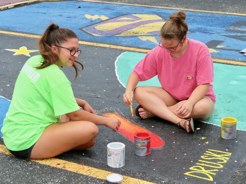 Westside Eagle Observer/RANDY MOLL Madi Powlowski and Dru Sikes work on some parking lot art on Thursday (Aug. 1, 2019) in preparation for the start of school at Gentry High School in two weeks. Not pictured but helping paint was Abi Powlowski.
