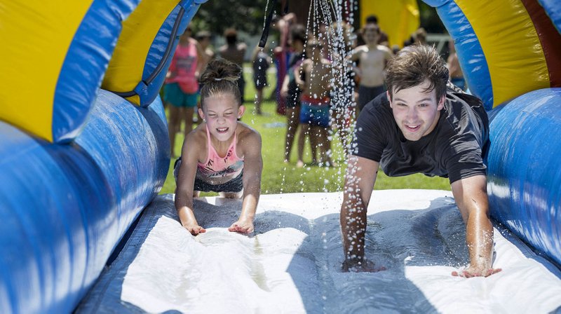 Taylor Fry, 11, of Rogers and Kyle Bowman, camp counselor, dive Tuesday onto a water slide during the Summer Day Camp at the Rogers Activity Center. This week's camp is the center's final session of the summer season. NWA Democrat-Gazette/BEN GOFF @NWABENGOFF