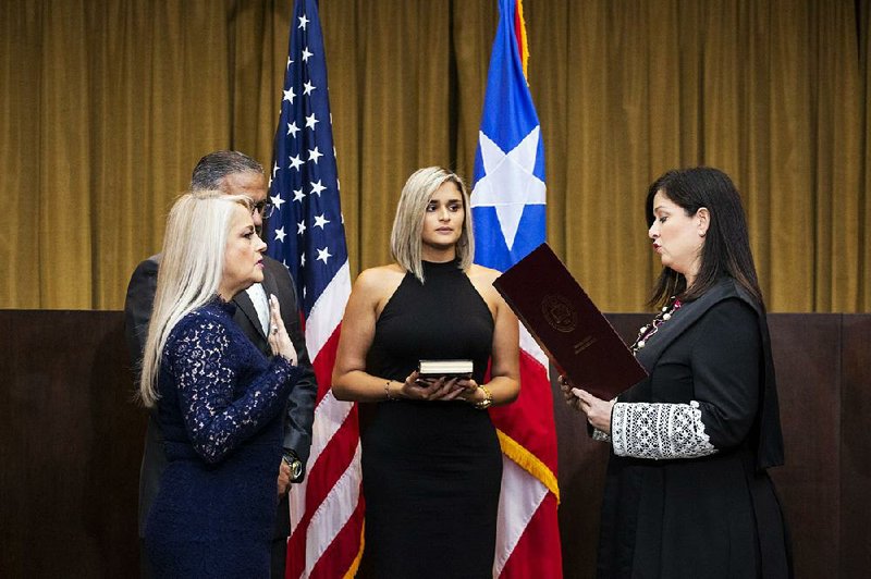 Wanda Vazquez (left), with her husband and daughter by her side, is sworn in Wednesday by Puerto Rico Chief Justice Maite Oronoz Rodriguez (right) in San Juan.