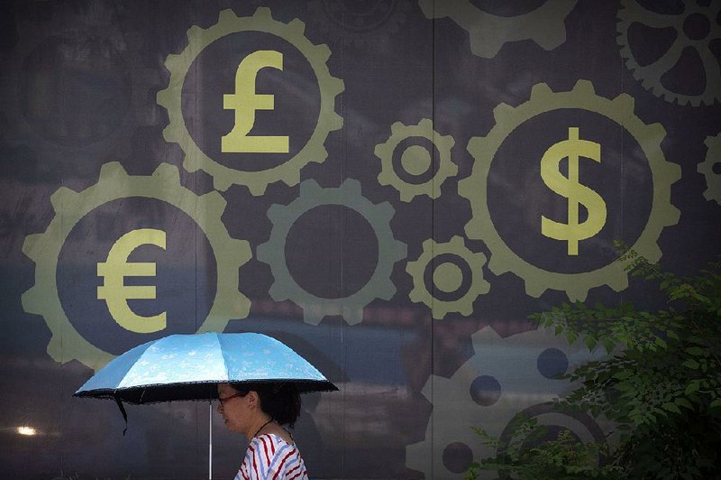 A woman walks past a mural displaying world currency symbols last month outside a bank in Beijing. The People’s Bank of China sets the yuan’s exchange rate each morning. 