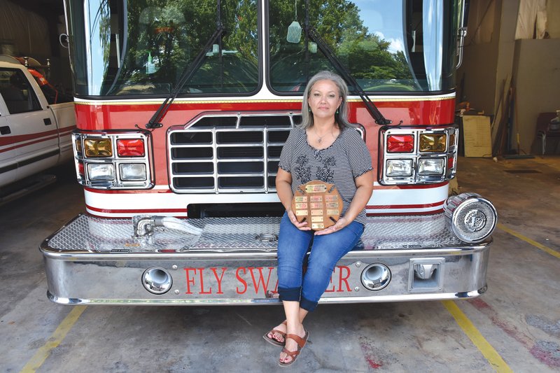 Aprill Reaves, a former volunteer firefighter, sits on a Ward Fire Department engine and holds an old plaque with names of donors to the ladies auxiliary, which became inactive in about 2002. Reaves re-established the Ward Fire Department Ladies Auxiliary and serves as its president. She said members and donors are needed. Her husband, Tony, was hired in February as the full-time fire chief. 