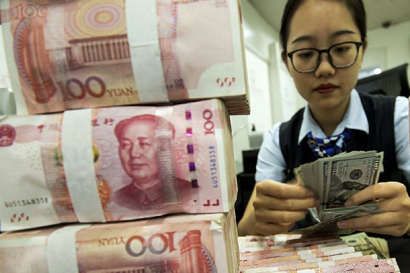 An employee counts U.S. currency next to stack of 100 Chinese yuan notes last week at a bank outlet in Hai’an in eastern China’s Jiangsu province. 