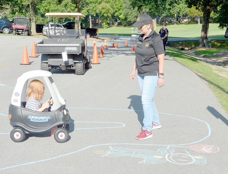 Keith Bryant/The Weekly Vista Chloe Bumgardner, 5, pilots a foot-propelled toy car through a chalk course with guidance from Bella Vista dispatcher Stacey Wigginton.