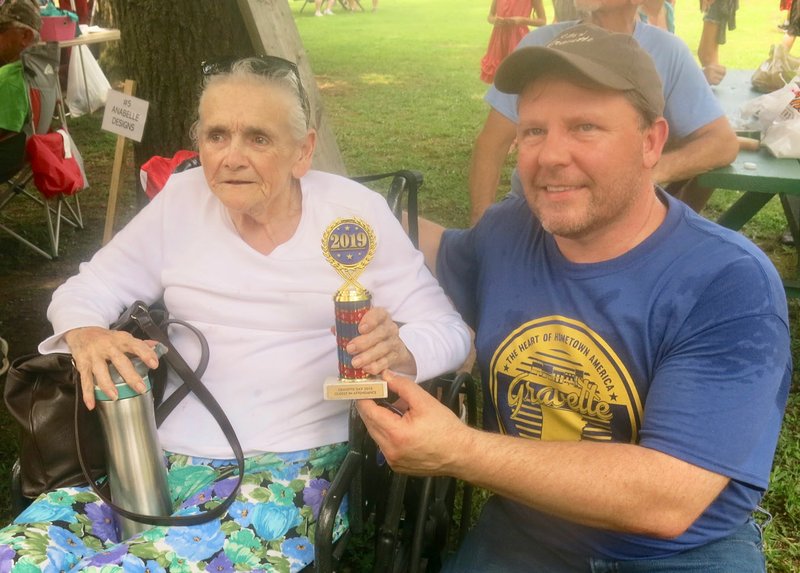 Westside Eagle Observer/SUSAN HOLLAND Gravette Mayor Kurt Maddox presents the trophy for the oldest person attending Gravette Day 2019 to Barbara Weeks, 84, of Gravette. The trophy was a well-deserved honor for braving the August heat to attend the city's annual celebration.