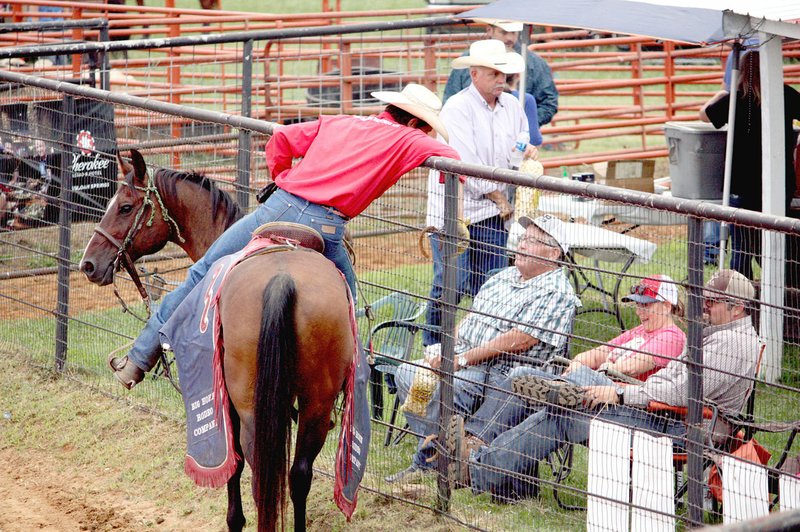 MARK HUMPHREY ENTERPRISE-LEADER A pickup man for Big Horn Rodeo Company, of Lamar, Okla., leans over the fence talking to fans during the 66th annual Lincoln Rodeo Saturday performance.