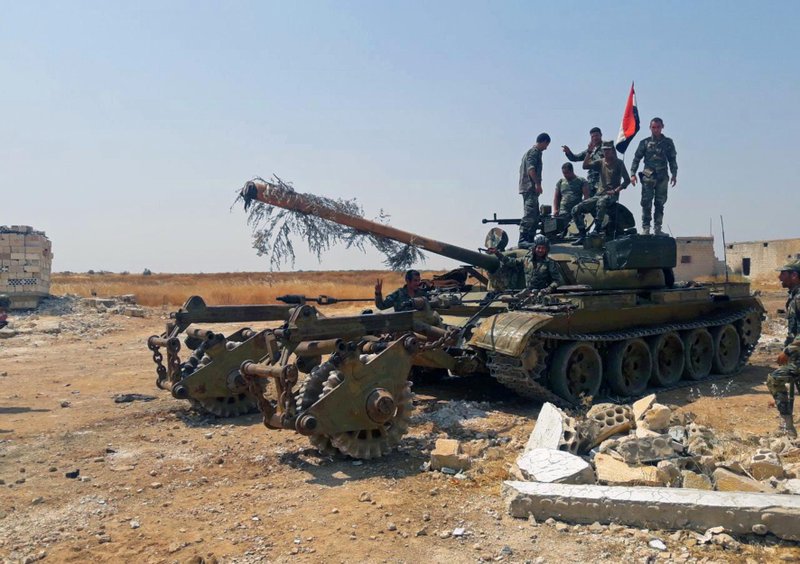 In this Tuesday, Aug. 13, 2019 photo, released by the Syrian official news agency SANA, Syrian army soldiers flash the victory sign as they stand on a tank, in northwestern Syria.  (SANA via AP)