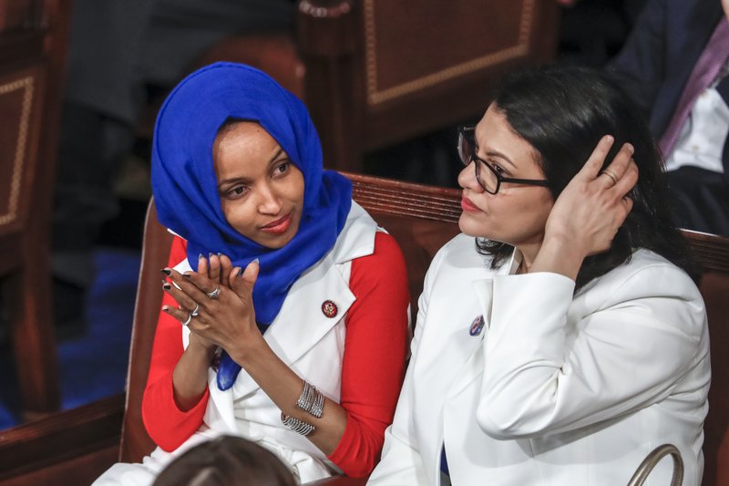 FILE - In this Feb. 5, 2019 file photo, Rep. Ilhan Omar, D-Minn., left, joined at right by Rep. Rashida Tlaib, D-Mich., listen to President Donald Trump's State of the Union speech, at the Capitol in Washington. (AP Photo/J. Scott Applewhite, File)


