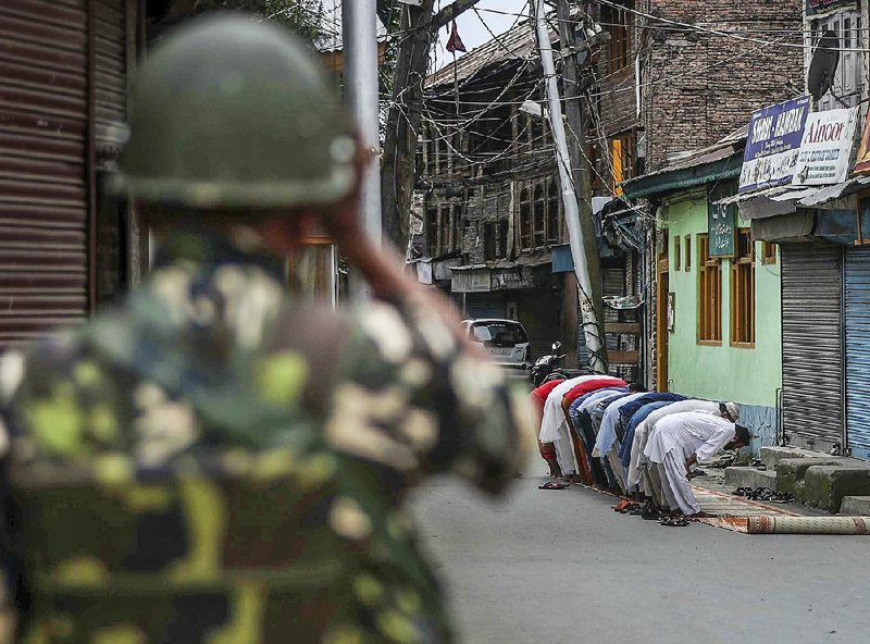 An Indian paramilitary soldier stands guard as Kashmiri Muslims offer prayers on a street outside a mosque Friday in Srinagar in India-controlled Kashmir. 