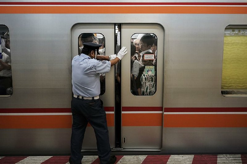 A station attendant pulls the door open for commuters crammed inside a train in Tokyo. The city’s transit system is running at double its capacity even before next summer’s Olympic crunch. 