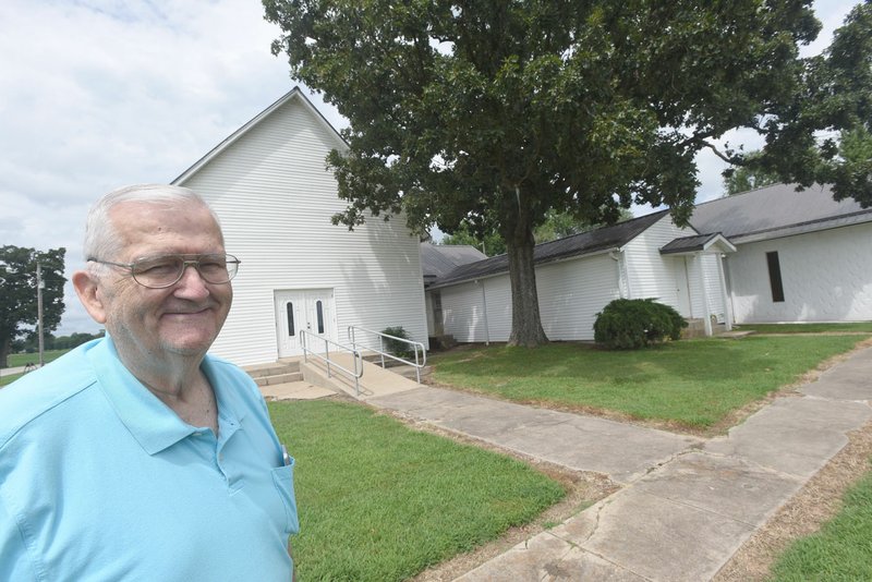 NWA Democrat-Gazette/FLIP PUTTHOFF Pat Robinson, pastor at Mason Valley Baptist Church, is eager to celebrate the church's 140th anniversary this weekend. The building at left is the original structure, Robinson says.