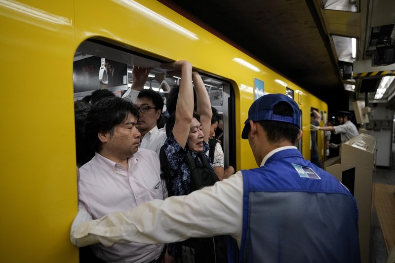 The Associated Press TIGHT FIT: In this July 30, 2019, photo, a station attendant watches as a commuter struggles to squeeze himself into an overcrowded train during morning rush hours at Akasaka Mitsuke Station in Tokyo. Tokyo has one of the most advanced public transport systems in the world, but with less than one year to go before the city hosts the 2020 Olympic Games, local governments, companies and commuters are bracing for unprecedented strain the events could put on rail transit and highways.