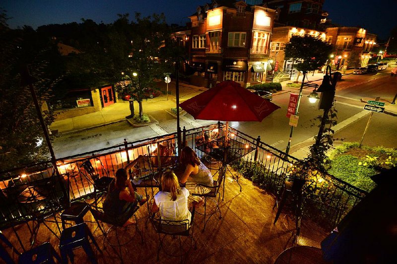 Friends Amy Garrett (from left), Heather Hanes and Bridget Kachel sit together Thursday atop the Dickson Street Pub as cars pass on Dickson Street in Fayetteville. The City Council plans to consider designating at least part of that street as being inside an entertainment district.