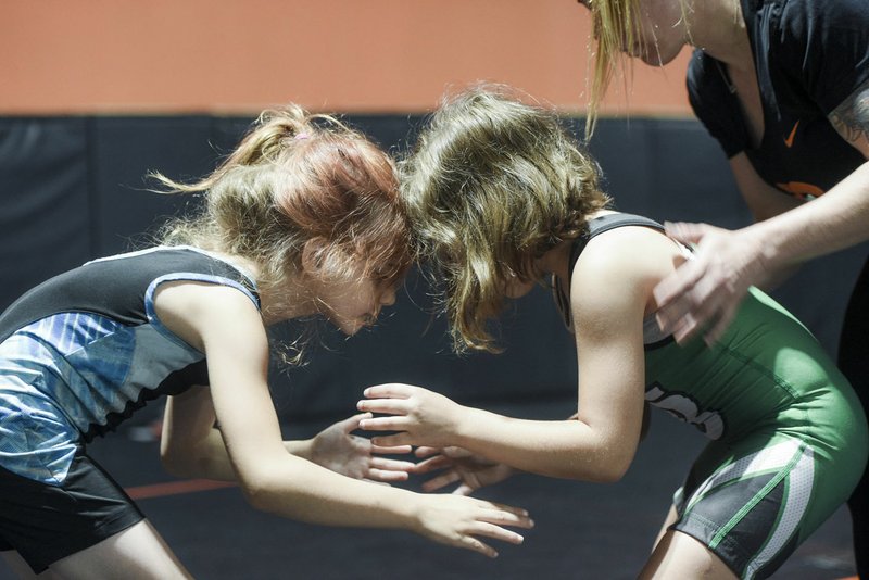 NWA Democrat-Gazette/CHARLIE KAIJO Eleora Robertson, 7, of Searcy and Teagen Loney, 7, of Van Buren (from left) wrestle with the help of Oklahoma national team coach Ashley Pagonis (right) during a women's wrestling camp held earlier in the summer at the Honey Badger Wrestling Club in Bentonville