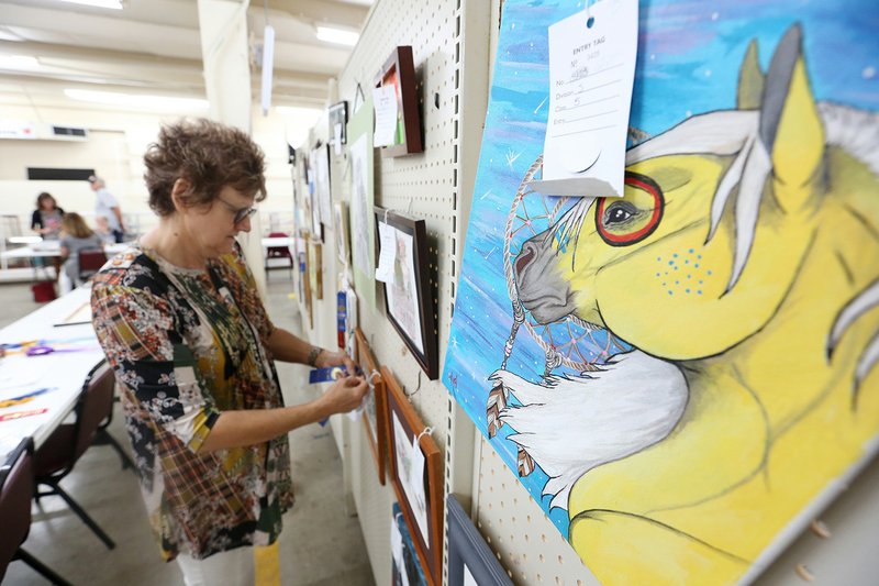 Sandy Perry, chairwoman of fine arts, attaches ribbons Monday to entries in the Adult Fine Art categories at the Washington County Fair in Fayetteville. The fair begins today and runs through Saturday. NWA Democrat-Gazette/DAVID GOTTSCHALK
