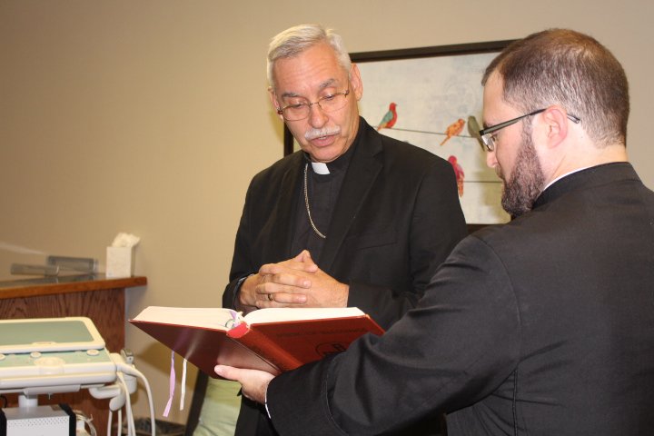 Ceremony: Fr. Eddie D'Almeida, right, assists as Bishop Anthony Taylor reads from the "Book of Blessings." Bishop Taylor blessed two new ultrasound machines at the Hannah Pregnancy Resource Center in a dedication ceremony Saturday afternoon. Caitlan Butler / News-Times