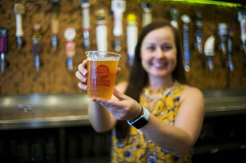 Olivia Klak, general manager of the Flying Saucer in Little Rock’s River Market district shows off the new open container that patrons can use, for a small charge, to imbibe alcohol on sidewalks and designated spaces when the entertainment district opens this evening. 