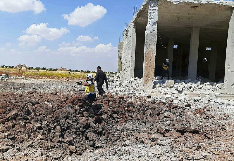 This photo provided by the Syrian Civil Defense White Helmets, shows a civil defense worker searching for victims under the rubble of a building that was hit by airstrikes Thursday in the northern town of Maaret al-Numan, in Idlib province, Syria. 