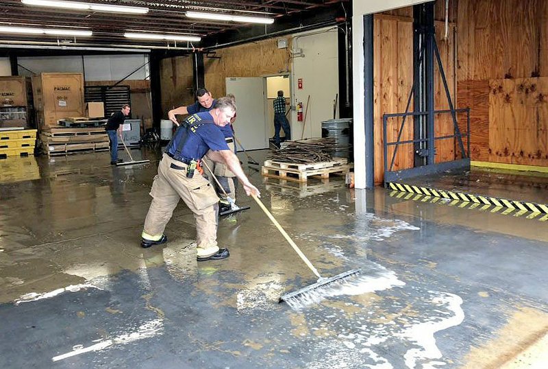 NWA Democrat-Gazette/STACY RYBURN Fayetteville firefighters help to push water out of a business Thursday in Fayetteville. A water main near the business ruptured shooting water into the business.