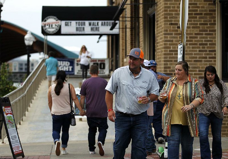 Brian Fulbright (from left), Brandi Wade and Amanda Fulbright, all of Batesville, cross President Clinton Avenue with beers in their hands Friday night in Little Rock’s new entertainment district, which allows people to drink alcohol from open containers in designated public areas.