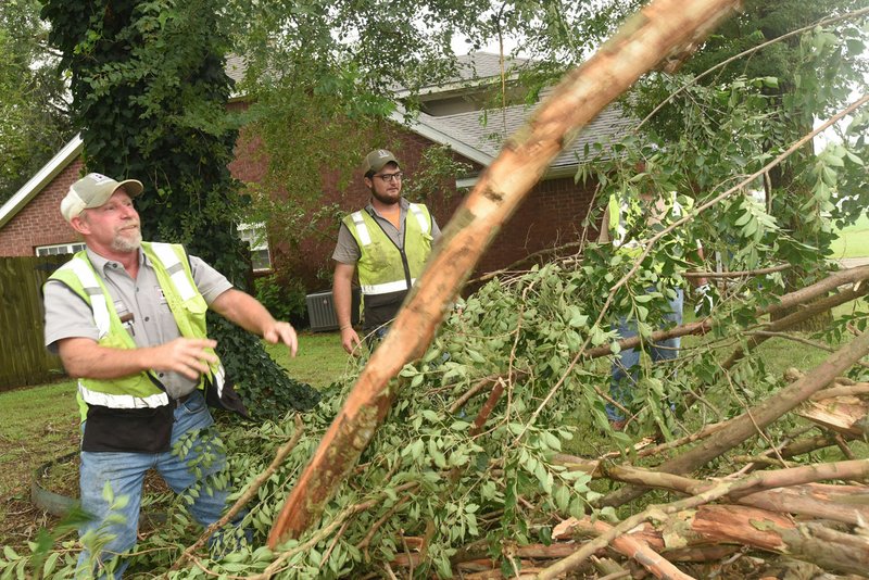 Rodney Chadwell (left) and Colter Keene with the Bentonville’s Street Department clear fallen tree limbs Tuesday in the wake of storms that happened late Monday. Street Department crews began clearing debris at 11 p.m Monday.