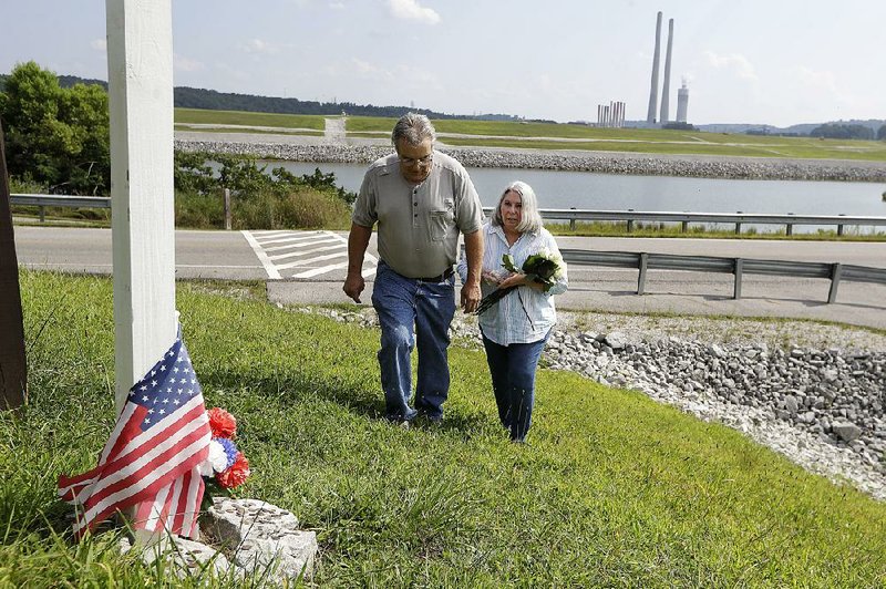 Ansol and Janie Clark visit a memorial near the Kingston Fossil Plant in Kingston, Tenn., which is visible in the background. The couple say the memorial is for workers who have experienced illnesses,  some fatal, after they helped clean up a coal ash spill at the plant in 2008.