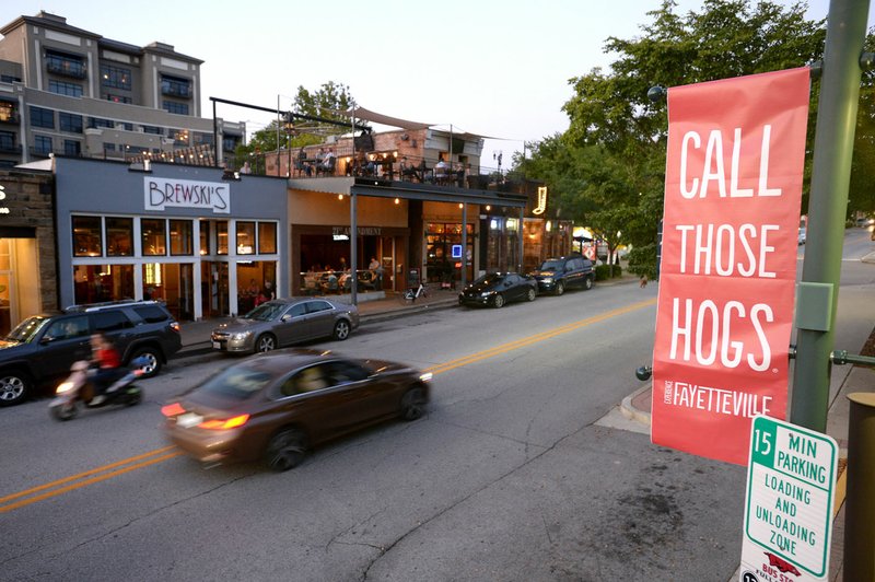 Motorists pass Aug. 15 as a small crowd of people gathers in bars on Dickson Street in Fayetteville.