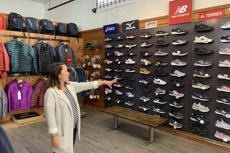 In this photo taken Wednesday, Aug. 28, 2019, Jennifer Lee, whose family owns Footprint shoe story in San Francisco, points to wall of athletic shoes, many of which are made in China and will be subject to new US tariffs on Chinese goods starting Sept 1. (AP Photo/Terry Chea)

