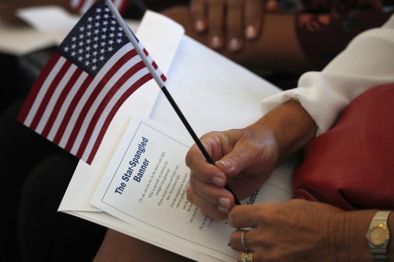 FILE - In this Aug. 16, 2019, file photo a citizen candidate holds an American flag and the words to The Star-Spangled Banner before the start of a naturalization ceremony at the U.S. Citizenship and Immigration Services Miami field office in Miami. U.S. Citizenship and Immigration Services officers can now create fictitious social media accounts to monitor information on foreigners seeking visas, green cards and citizenship.(AP Photo/Wilfredo Lee)