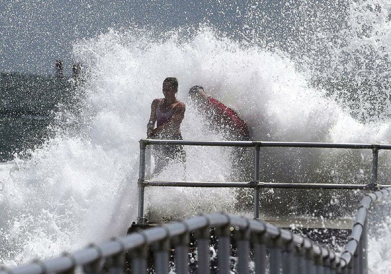 People in Ponce Inlet, Fla., cling to a railing Monday as a wave crashes into the jetty at Lighthouse Point Park. Hurricane Dorian is forecast to remain offshore as it moves toward the U.S.’ East Coast, but Florida has ordered evacuations in some vulnerable areas. 