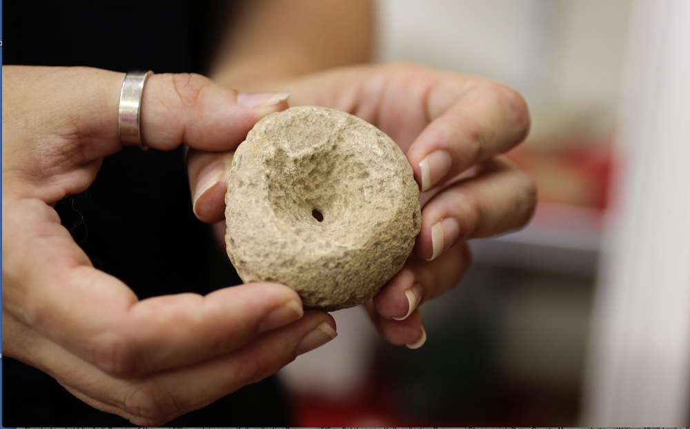 Lydia Rees holds a stone disc that was used by Mississippian people to play a competitive game of skill, rolling the disc and throwing spears at it. The artifact is at the Desha County Museum. Rees is Archeological Survey Station Assistant Archeologist.