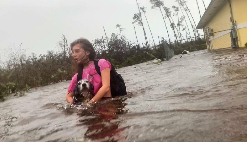 Julia Aylen carries her dog from her flooded home Tuesday in Freeport, Bahamas, as rescuers arrive. Marvin Dames, minister of national security, said Hurricane Dorian caused “a crisis of epic proportions.” 