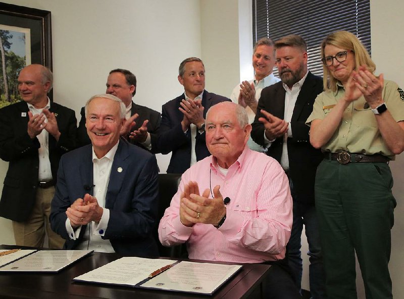 Gov. Asa Hutchinson (seated left) sits Wednesday in Little Rock beside U.S. Secretary of Agriculture Sonny Perdue after they signed a cooperative agreement between the U.S. Department of Agriculture and certain state agencies.