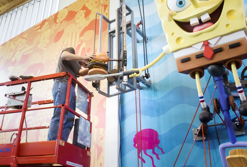 Dustin Griffith, lead exhibits developer, cleans and tunes Thursday the krabby patty of the giant SpongeBob SquarePants puppet during the annual Fall Refresh at the Amazeum in Bentonville. The Amazeum will be closed today for the all-hands-on-deck, cleaning and maintenance to improve the facility. All full and part-time staff participate in a deep cleaning. Staff also took down the temporary exhibit "Forever Forest" to make way for its new installment "Toys: The inside story." NWA Democrat-Gazette/CHARLIE KAIJO