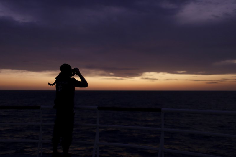 A member of SOS Mediterranee's Search and Rescue team monitors the horizon at dawn with binoculars for potential boats in distress from aboard the Ocean Viking in international waters north of Libya, Sunday, Sept. 8, 2019. The humanitarian rescue ship jointly operated by SOS Mediterranee and Doctors Without Borders is conducting its second search and rescue mission in the Central Mediterranean. (AP Photo/Renata Brito)