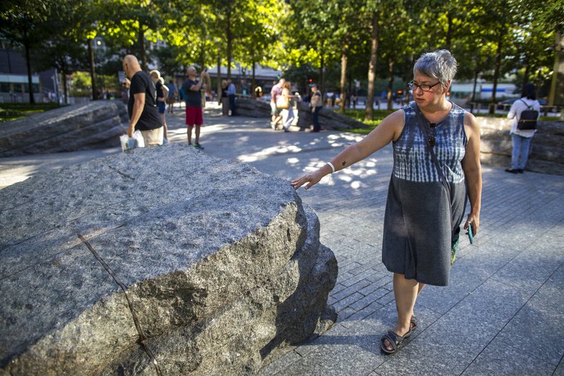 In this Thursday, Aug. 29, 2019, photo a visitor touches one of the granite slabs at the 9/11 Memorial Glade at the National September 11 Memorial &amp; Museum in New York. When the names of nearly 3,000 Sept. 11 victims are read aloud Wednesday, Sept. 11 at the World Trade Center, a half-dozen stacks of stone will quietly salute an untold number of people who aren't on the list. The granite slabs were installed on the memorial plaza this spring. They recognize an initially unseen toll of the 2001 terrorist attacks: firefighters, police and others who died or fell ill after exposure to toxins unleashed in the wreckage. (AP Photo/Mary Altaffer)