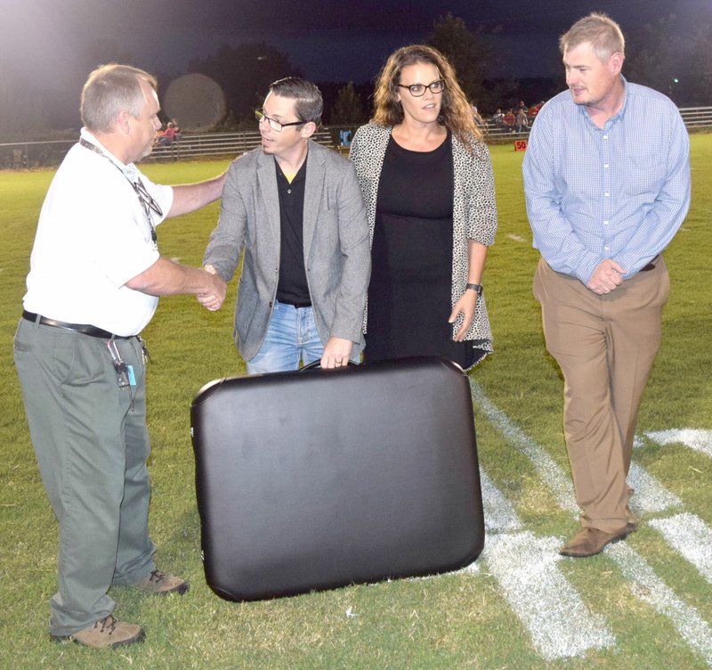 Westside Eagle Observer/MIKE ECKELS Toby Conrad (left), Decatur athletic director, accepts one of two portable treatment/sideline tables donated by Brad and Ladale Clayton as Steve Watkins, Decatur superintendent, looks on during halftime of the Decatur-Watts, Okla., eight-man football contest at Bulldog Stadium in Decatur on Aug. 30.