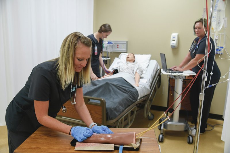 NPC nursing students Ashley Allison, left, Annie McWilliams, and Christie Welch demonstrate how they use some of the equipment int the National Park College nursing lab. -Photo by Grace Brown