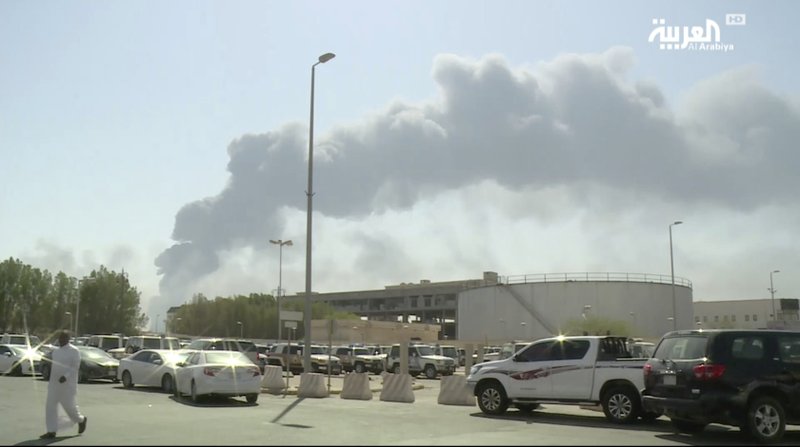 In this image made from a video broadcast on the Saudi-owned Al-Arabiya satellite news channel on Saturday, Sept. 14, 2019, a man walks through a parking lot as the smoke from a fire at the Abqaiq oil processing facility can be seen behind him in Buqyaq, Saudi Arabia. Drones launched by Yemen's Houthi rebels attacked the world's largest oil processing facility in Saudi Arabia and another major oilfield Saturday, sparking huge fires at a vulnerable chokepoint for global energy supplies. (Al-Arabiya via AP) TV OUT NO SALES