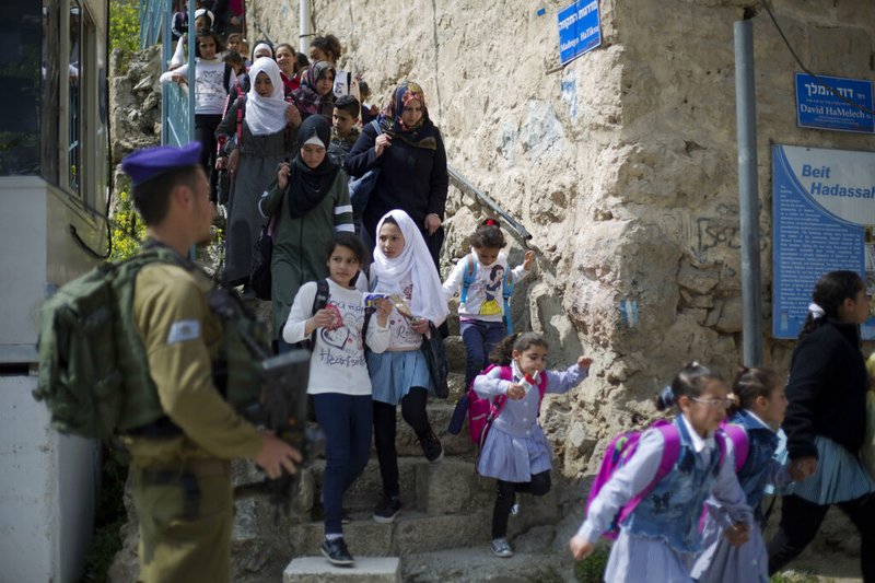 FILE - In this March 21, 2019 file photo, an Israeli solider stands guard as Palestinian school children cross back from school in the Israeli controlled part of the West Bank city of Hebron. Israeli Prime Minister Benjamin Netanyahu vowed Monday Sept. 16, 2019, to annex "all the settlements" in the West Bank, including one in Hebron, an enclave deep in the heart of the largest Palestinian city, in a last-ditch move that appeared aimed at shoring up nationalist support the day before a do-over election. (AP Photo/Ariel Schalit, File)