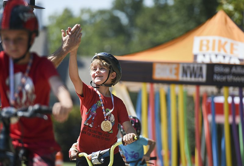 Volunteer Scott Fitzgerald of Buddy Pegs (not shown) high-fives Tegan Johnson, 9, of Rogers (center) during an Open Streets event, Sunday on South Fifth Street and West Cherry Street in Rogers. BikeNWA hosted Open Streets Rogers, a festival with vendors, music and all things bikes. The goal of Open Streets is to promote an active lifestyle through a series of free bike events held across the region, opening public spaces to walking, biking, skating and discovering active transportation. NWA Democrat-Gazette/CHARLIE KAIJO