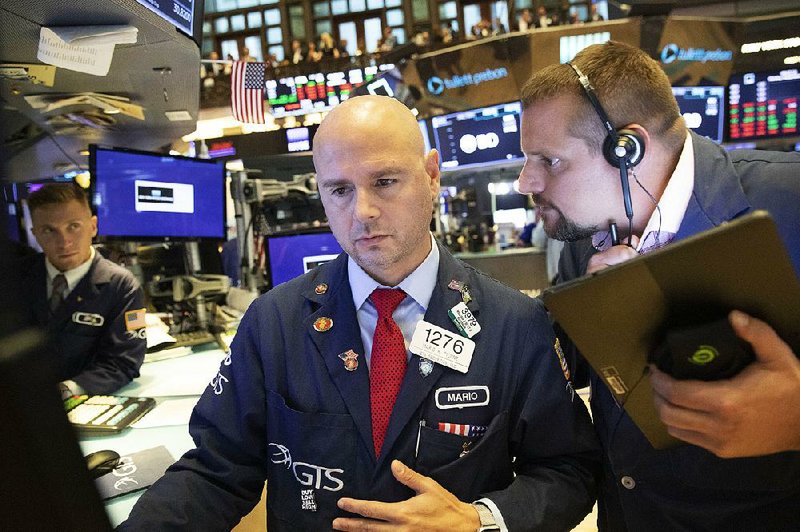 Mario Picone (center) and Michael Milano (right) work Monday on the floor of the New York Stock Exchange. Stocks fell after a weekend attack on Saudi Arabia’s biggest oil processing facility caused crude prices to surge. 