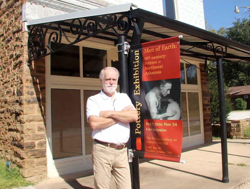 LYNN KUTTER ENTERPRISE-LEADER Lawrence McElroy, director of arts and culture for Historic Cane Hill, stands next to the banner announcing the next exhibit for The Museum Gallery at Historic Cane Hill. An exhibit on 19th century potters of Northwest Arkansas opens Sept. 21 during the 33rd Cane Hill Harvest Festival.