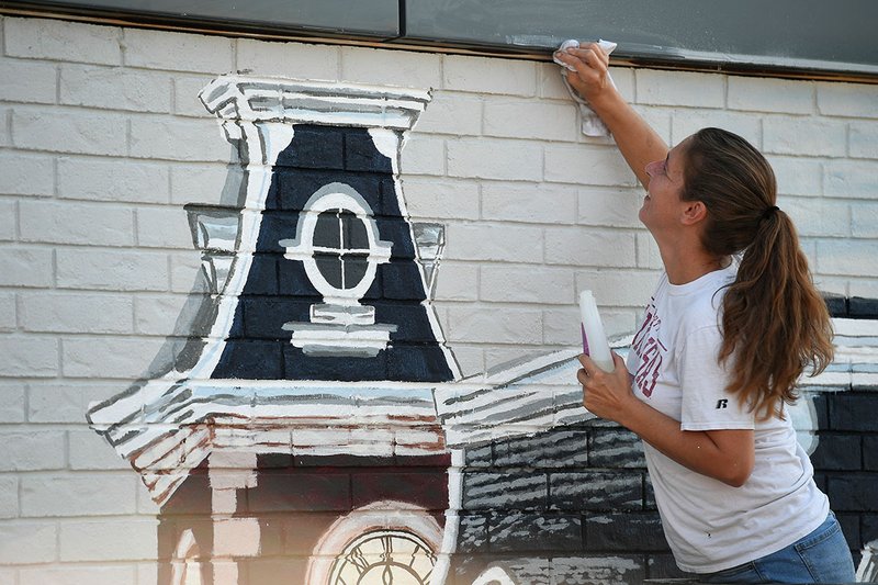 Jennifer Wall of Springdale cleans tape residue Wednesday off of the border of a mural she painted on a west Fayetteville business. The 550-square-foot mural is a tribute to Fayetteville and includes scenes from the Fayetteville Farmers Market and Old Main on the University of Arkansas campus. Wall specializes in windows and wall murals. For information, contact Wall at wallartjen@gmail.com NWA Democrat-Gazette/J.T. WAMPLER